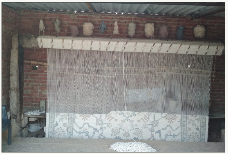 Traditional carpet loom with partially woven rug, yarn spools, at Bhadohi Carpets House workshop