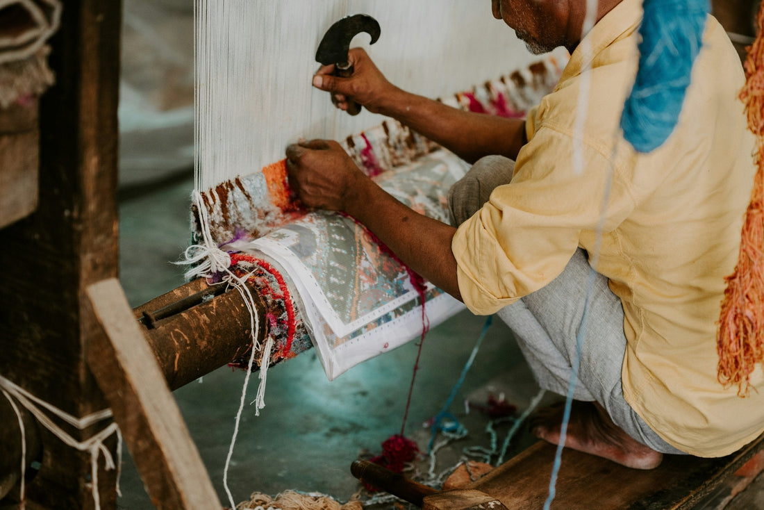 Artisan weaving a traditional Bhadohi carpet by hand on loom, yarns visible, India