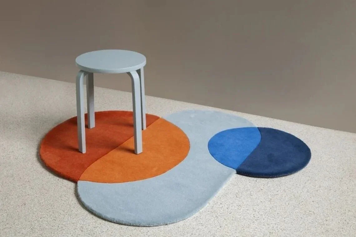 Modern irregular Bhadohi Carpets House rug in orange, blue, and grey with round stool on top