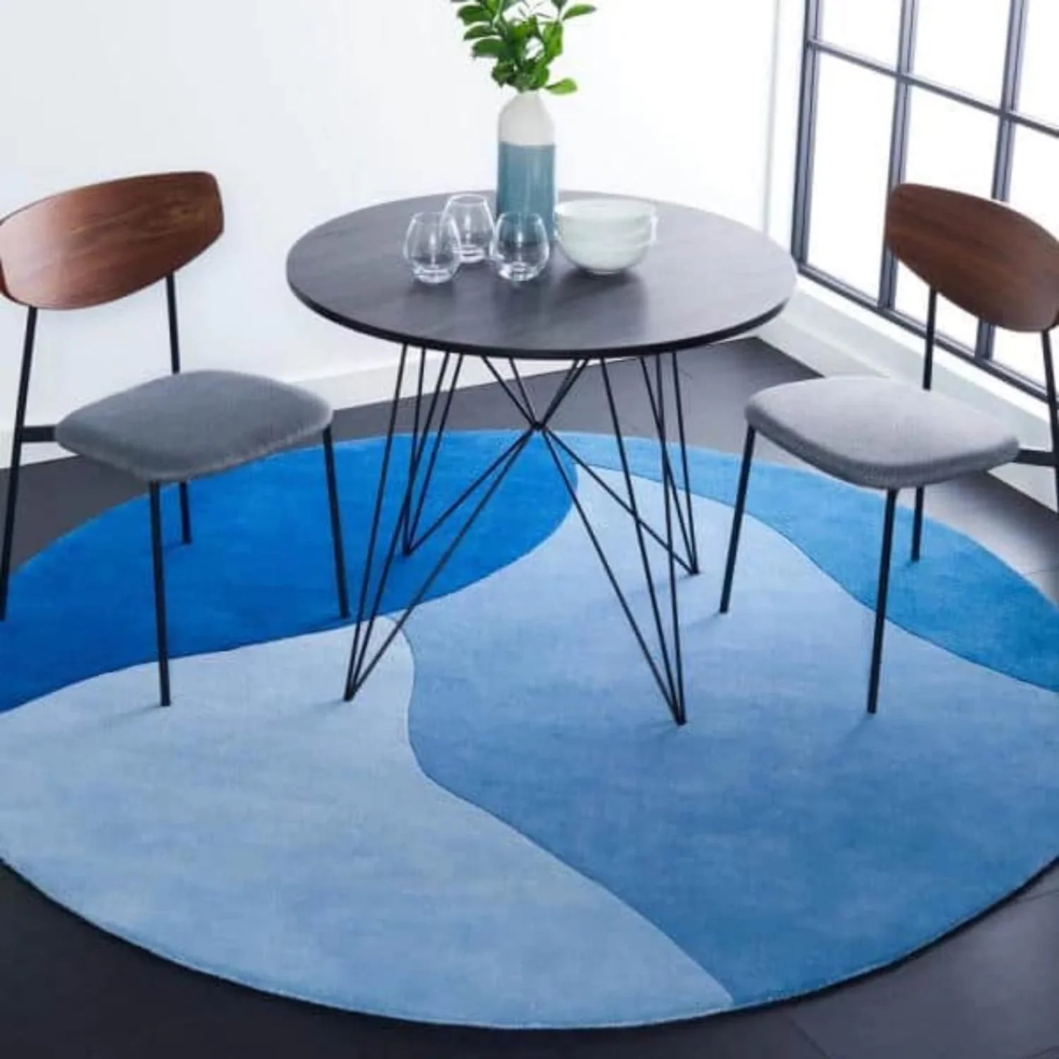 Modern round wool carpet rug in blue hues under a black dining table with two chairs, Bhadohi Carpets House