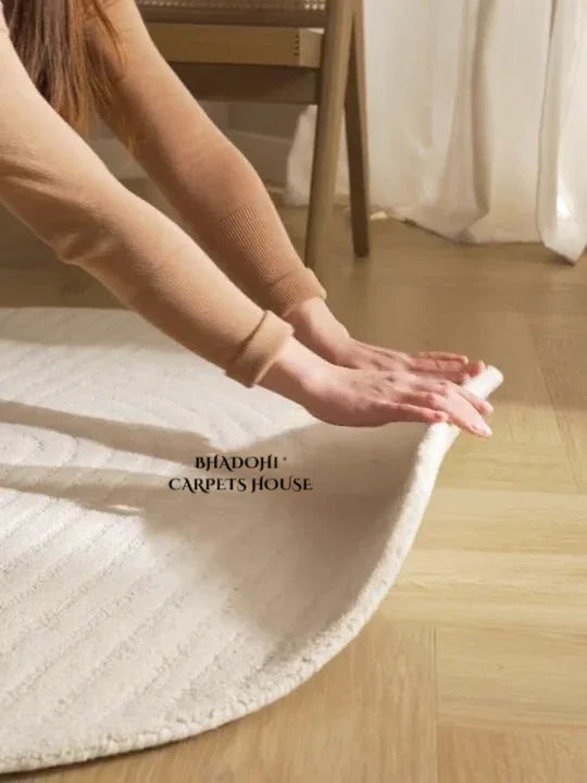 Hand smoothing a round white wool carpet on wooden floor, Bhadohi Carpets House rug