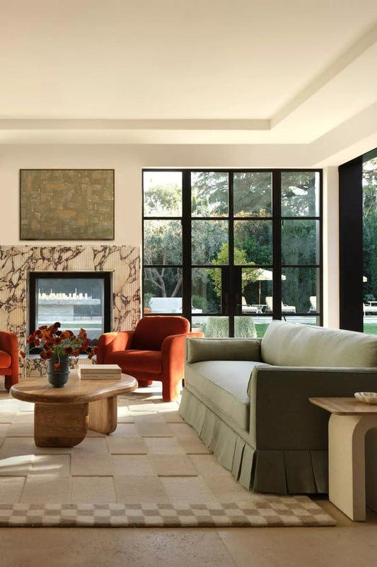 Modern living room with large windows, cut loop carpet rug, green sofa, red chairs and wooden table from Bhadohi Carpets House.